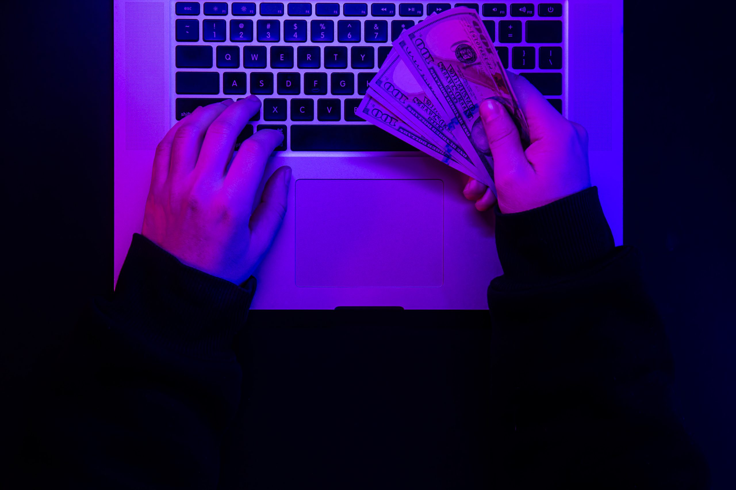 top down view of hands holding money over laptop keyboard