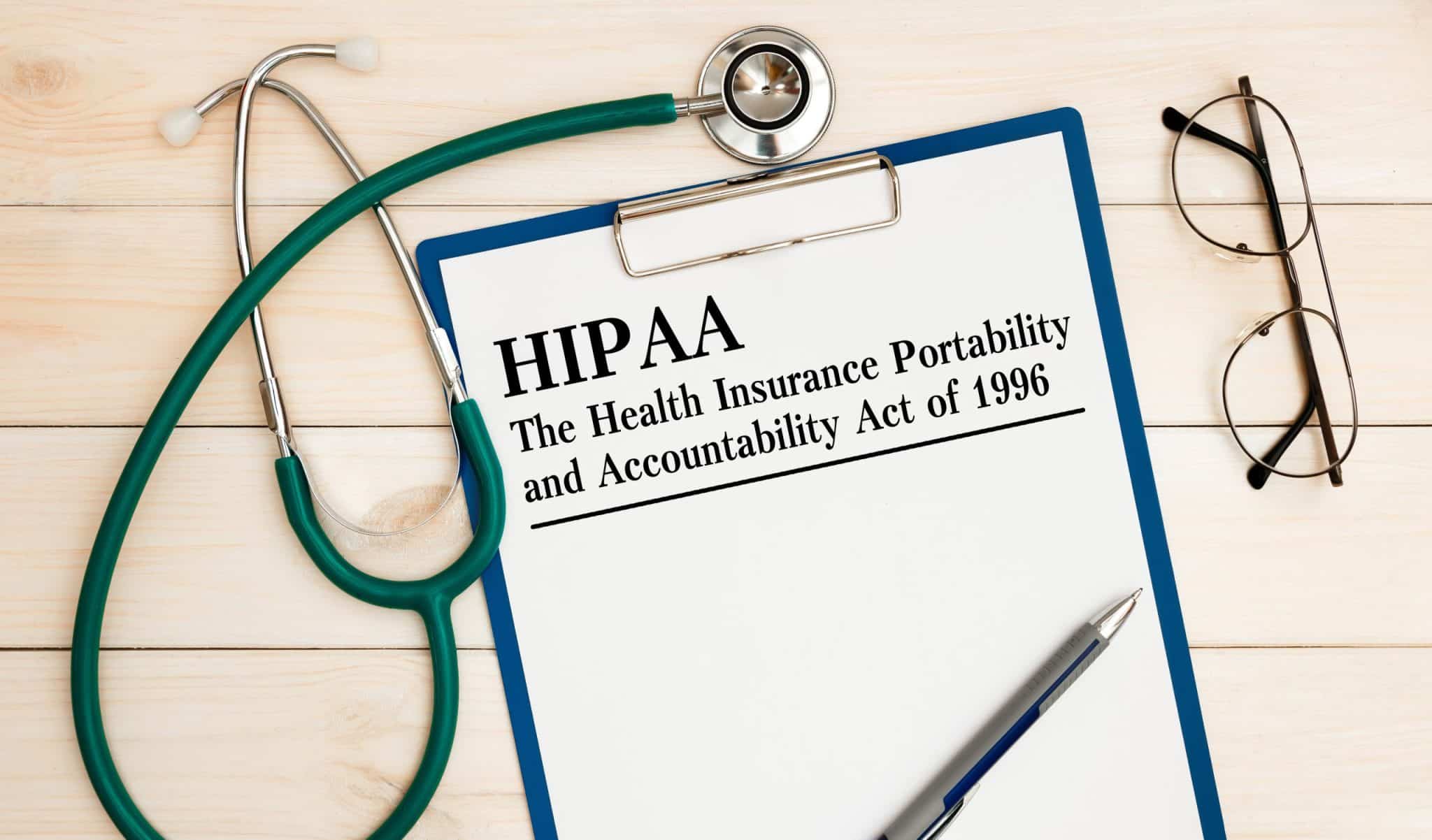 HIPAA compliance on a clipboard surrounded by a stethoscope, glasses, and a pen