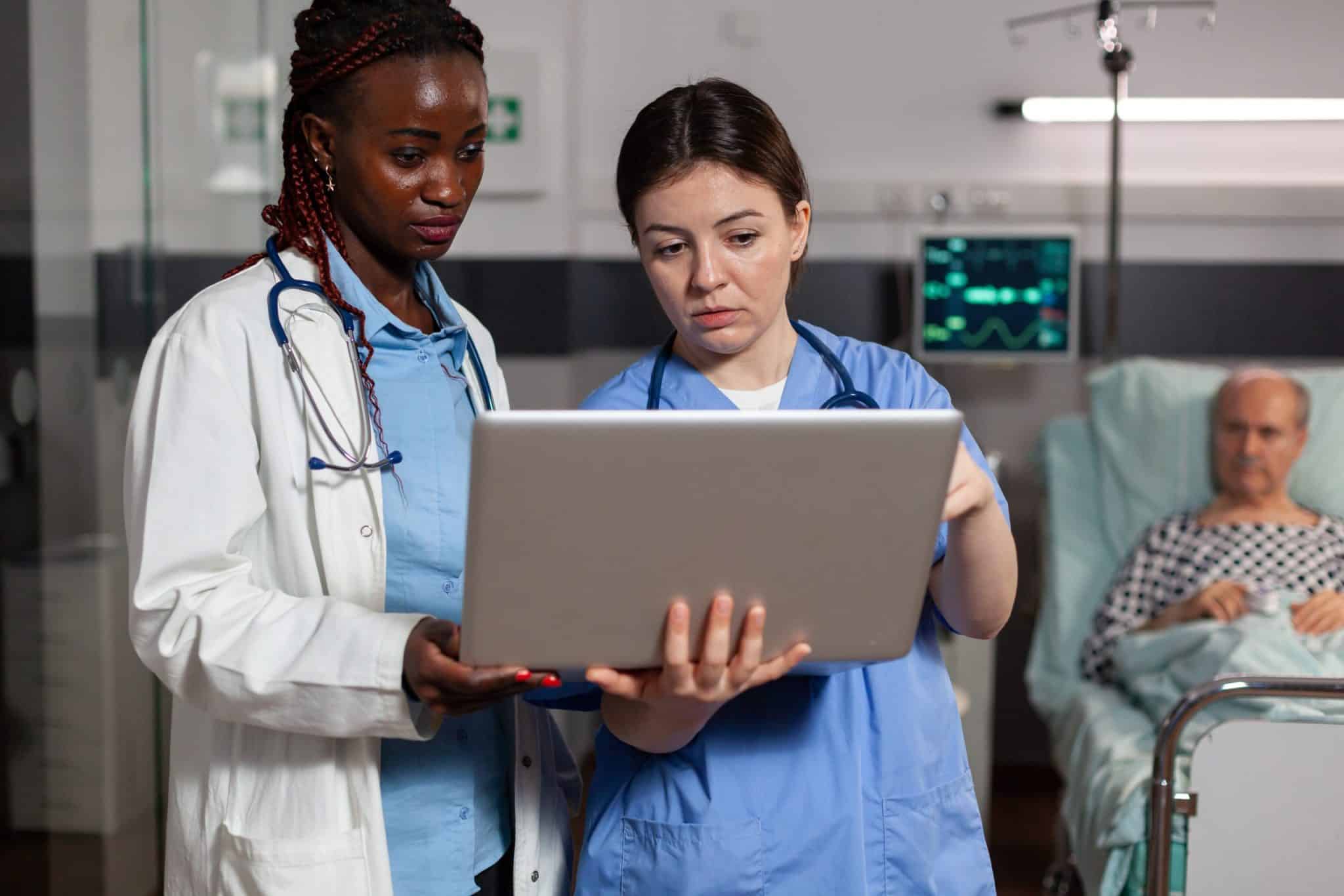 Doctor and nurse discuss results on a laptop with a blurred patient in the background