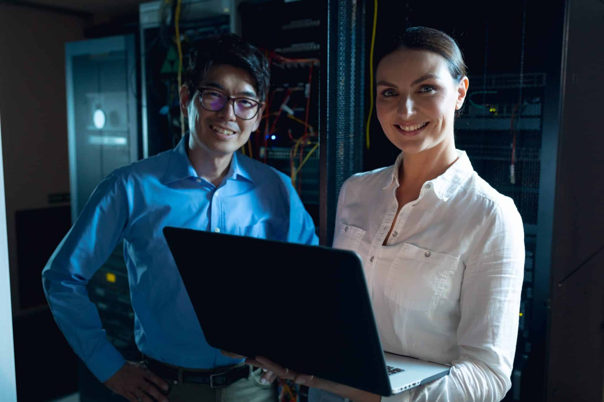 male and female engineers with laptop smiling in computer server room.