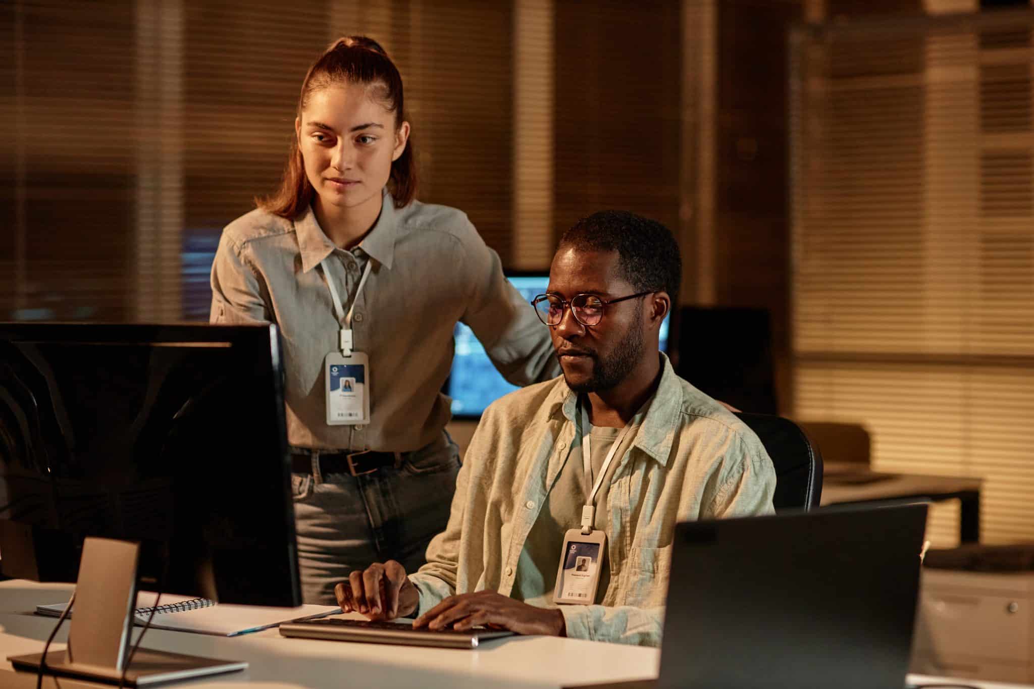 Portrait of two software developers man and woman looking at computer screen together in dark office