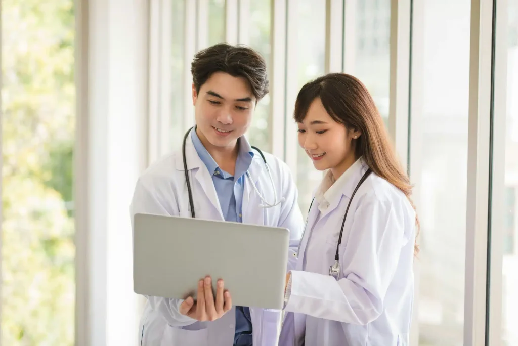 group-of-asian-doctors-team-portrait-standing-and-using-laptop-with-other-colleagues-in-background-